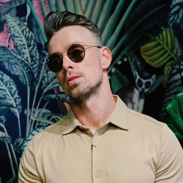 Stylish men's accessories showcased by a man wearing sunglasses against a tropical backdrop.