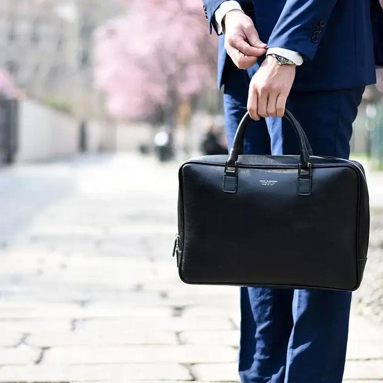 A stylish man wearing a suit holding a black bag, representing men bags collection.