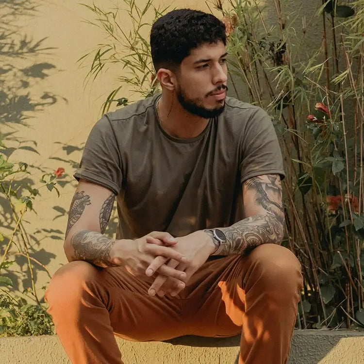 Casually dressed man with tattoos sitting outdoors, showcasing trendy men clothing.