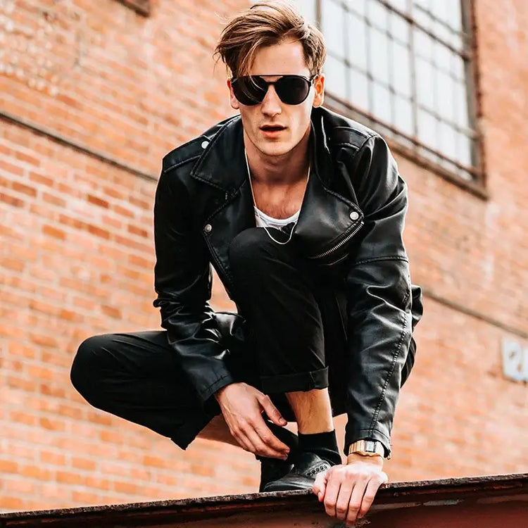 Stylish man's outfits featuring a man in a leather jacket and sunglasses crouching on a railing.