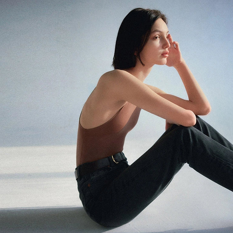 Women clothing model wearing a brown bodysuit and black jeans, showcasing modern women's fashion.